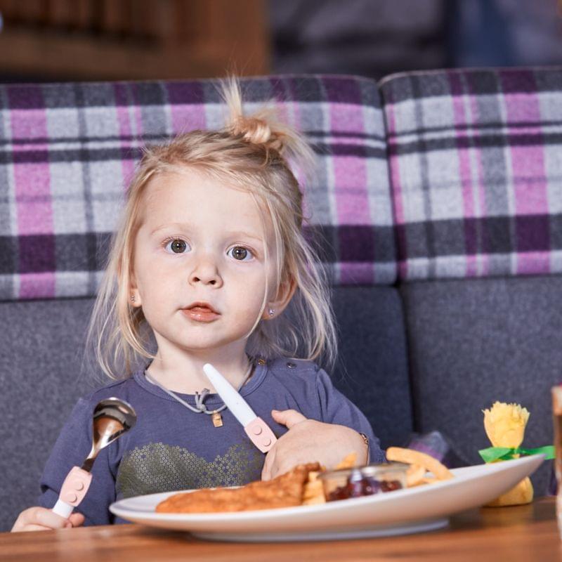 Blonde toddler eating French fries and chicken at restaurant table